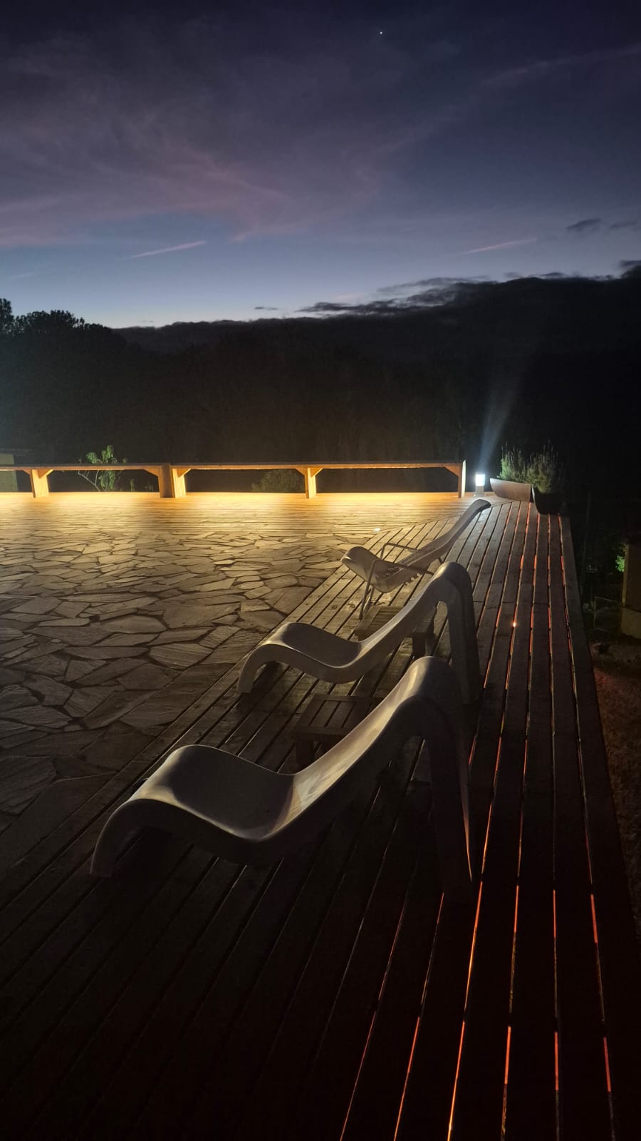 Deck iluminado à noite com espreguiçadeiras e vista para a natureza