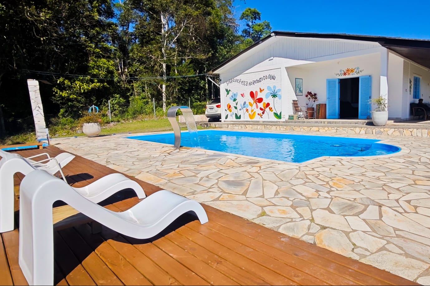 Piscina com cascata, deck de madeira e a casa ao fundo